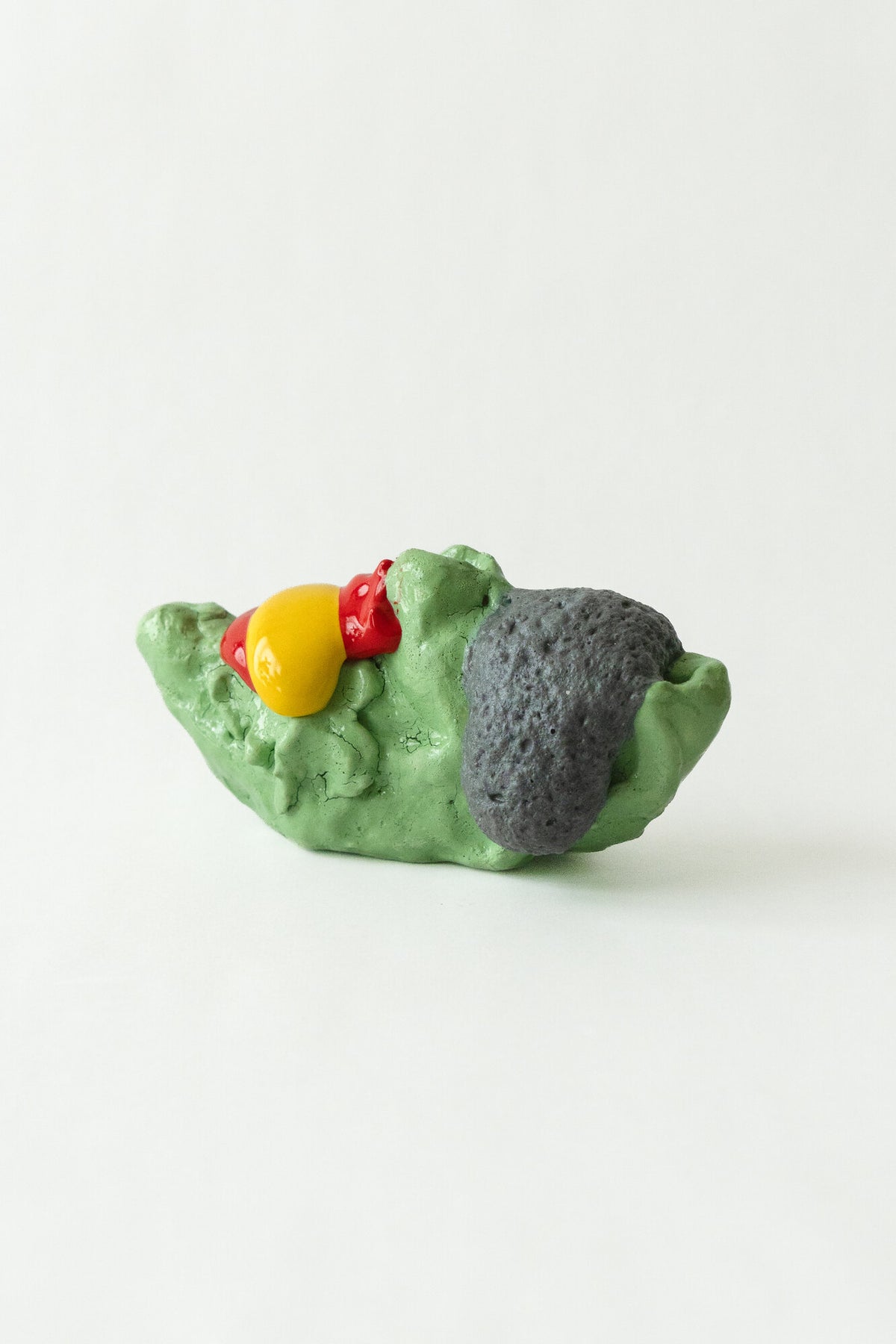 Foam #9 by Onree: Low green ceramic form with a dark textured section and glossy red and yellow additions — full view