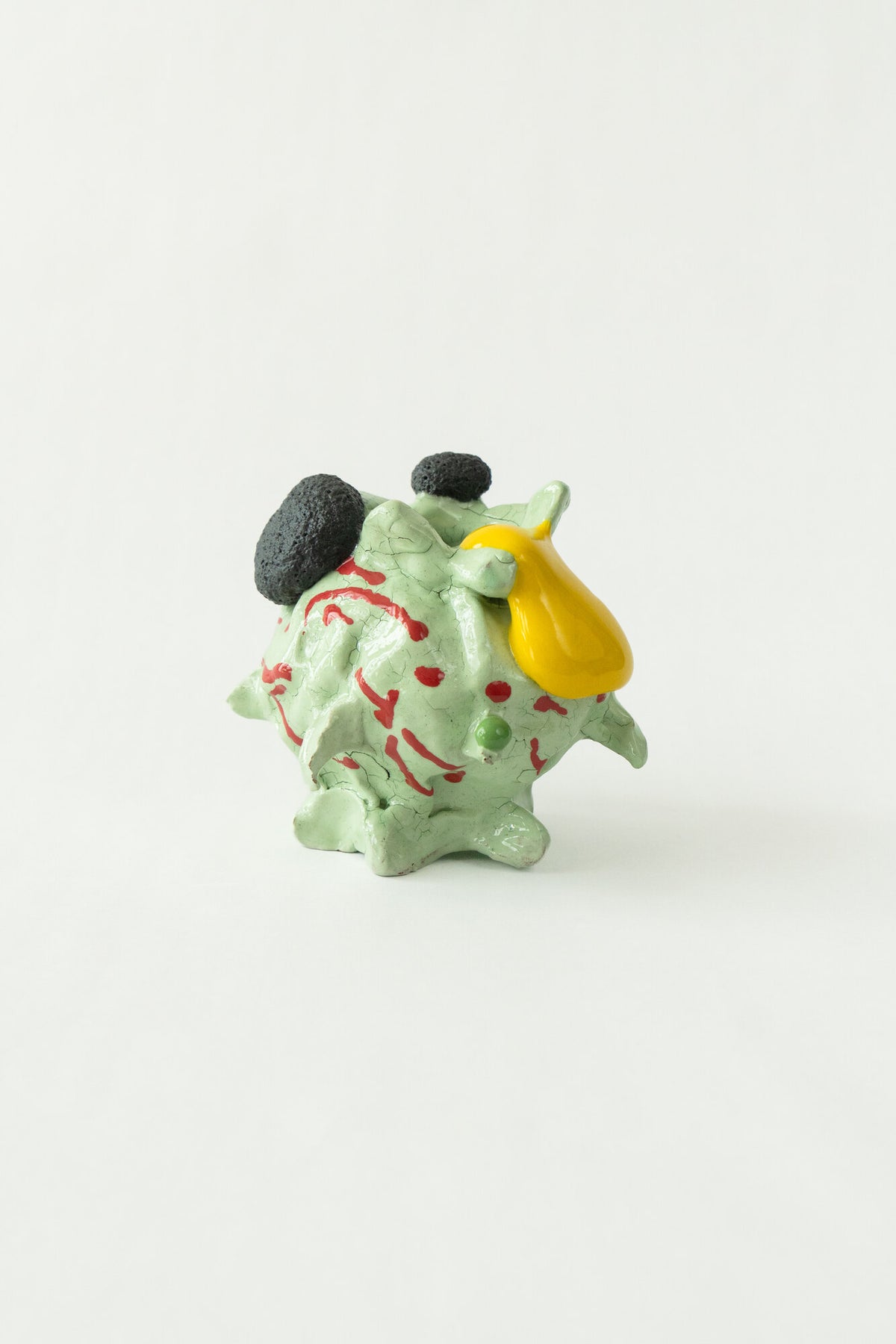 Foam #23 by Onree: Pale green ceramic vessel with red marks, dark textured circles and a yellow glazed detail — full view